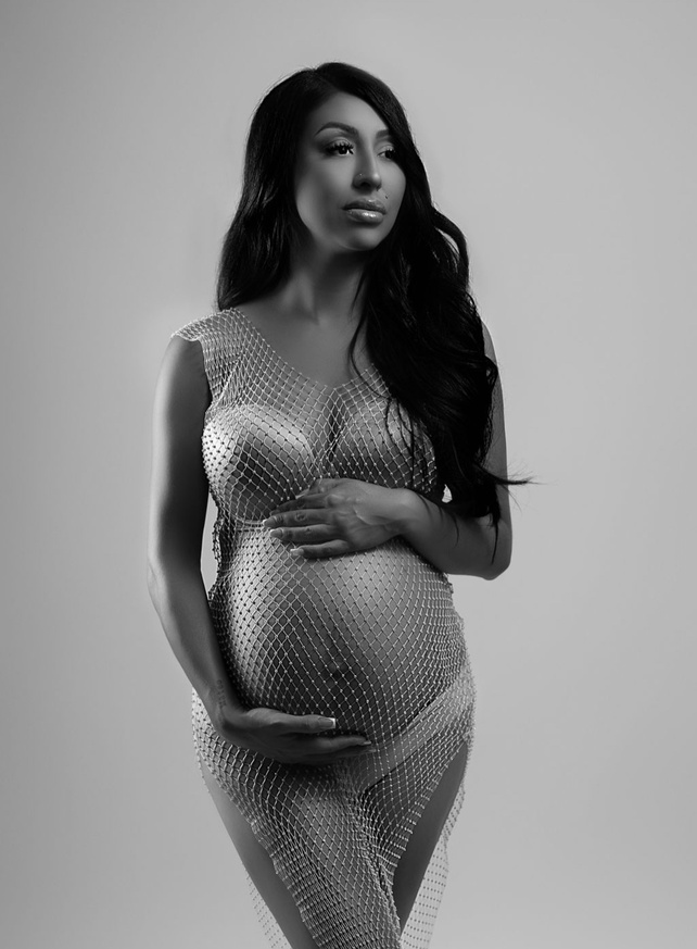 gorgeous monochromatic black and white maternity image. She has a standing pose and is wearing a white and diamond fishnet dress found on amazon taken by Modesto California's best studio photographer. She is known for bold and dramatic work.