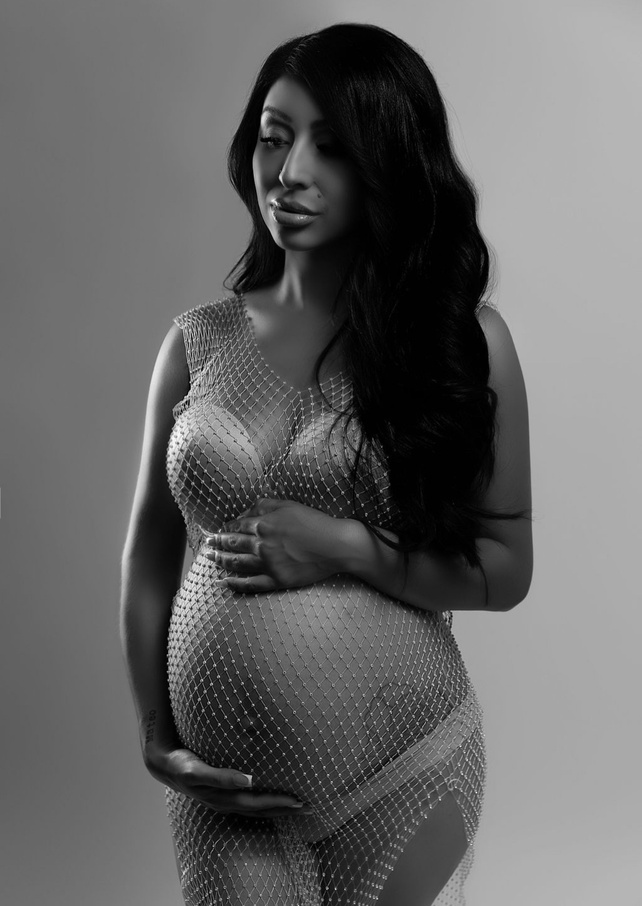 gorgeous monochromatic black and white maternity image. She has a standing pose and is wearing a white and diamond fishnet dress found on amazon taken by Modesto California's best studio photographer. She is known for bold and dramatic work.