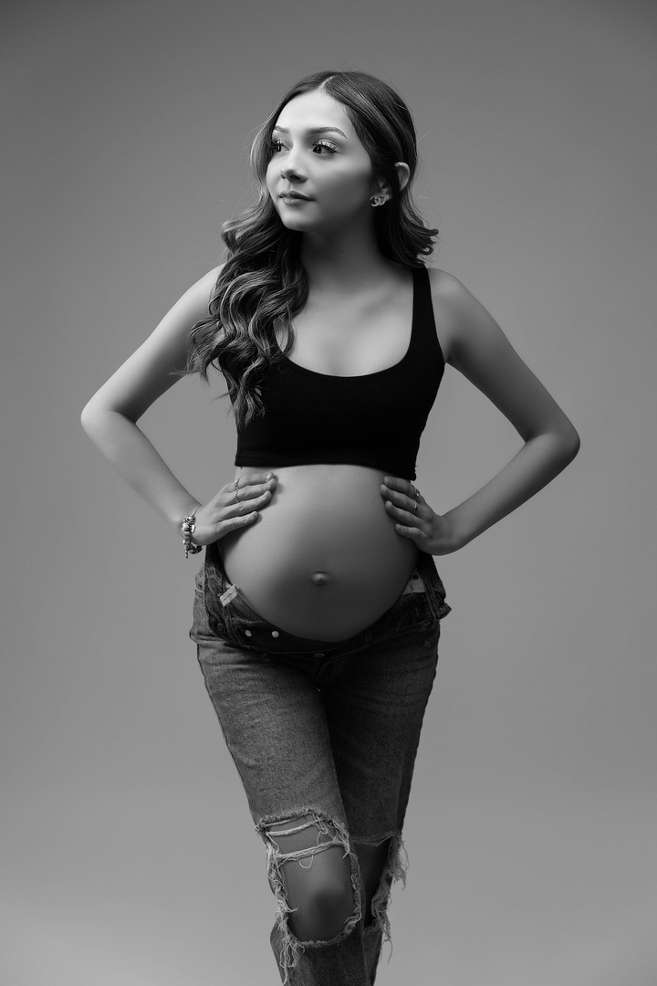 gorgeous young mother with open jeans and a black top exposing her pregnancy belly in a high fashion pose. this portrait was edited in black and white for a timeless luxury look Clavin Klein inspired photography 